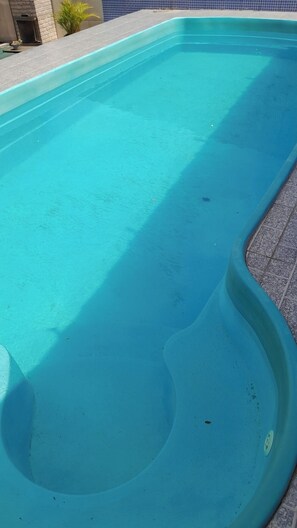 Piscina com borda azulejada e parede de pedra ao fundo.