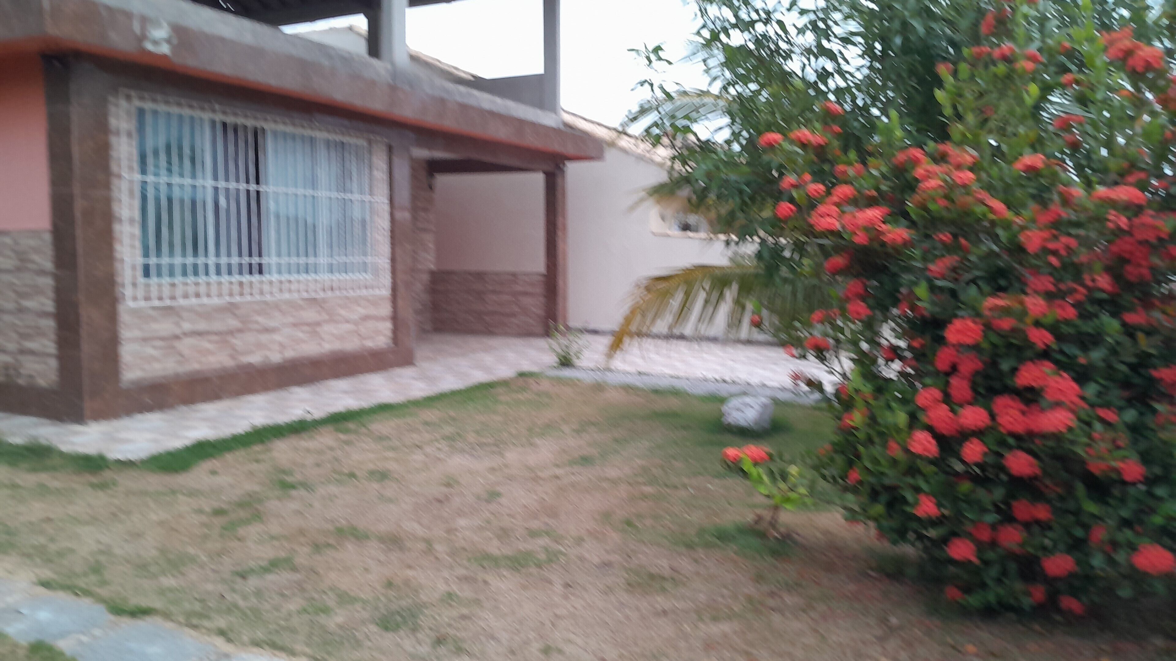 Ein Haus mit einer Veranda, einem kleinen Garten und einem Strauch mit roten Blüten.