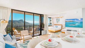 A spacious room with a balcony, a bed, a dining table set, and a large window with a mountain view.