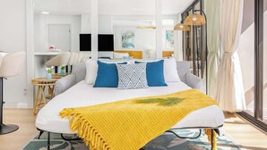 A modern hotel room with a large bed, a desk, and a view of the city.