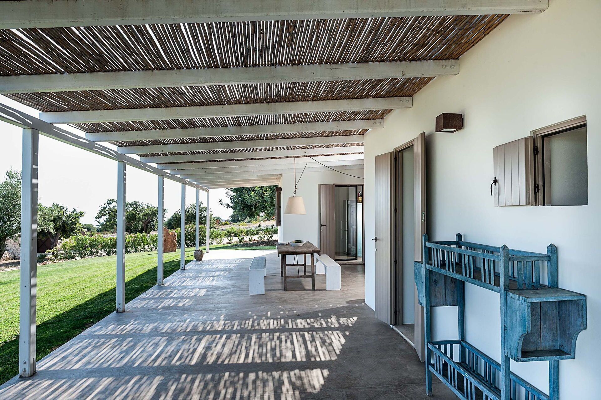 A covered outdoor area with a concrete floor, a table, and chairs, leading to a glass door.