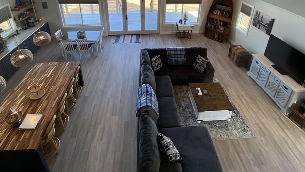 A spacious loft with a high ceiling, a large dining area, a cozy seating area with a sofa and TV, and a view of the ocean through large windows.