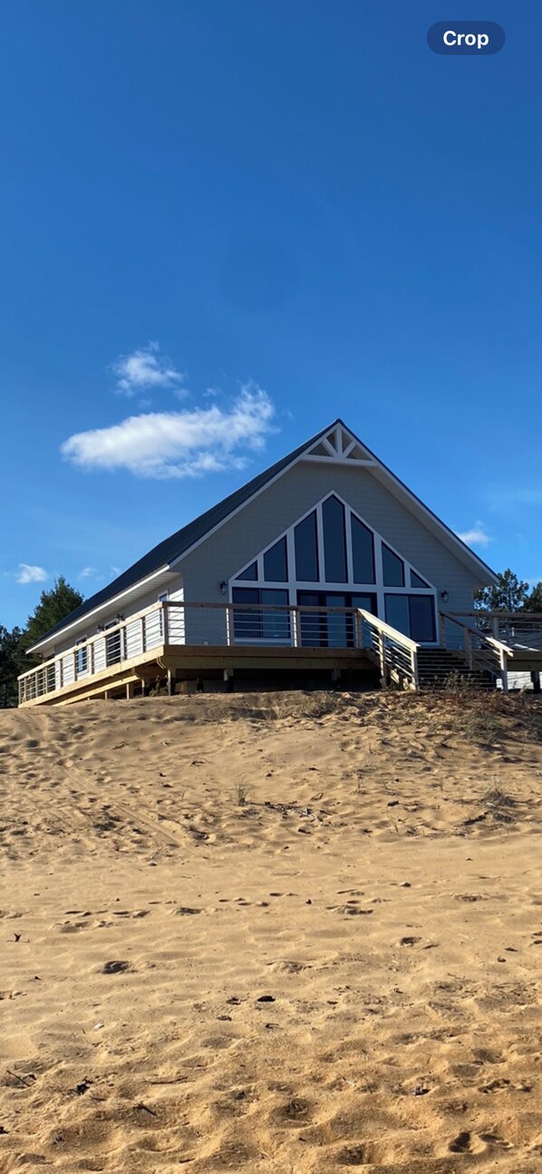 A large, single-story building with a prominent gable roof, situated on a sandy terrain.
