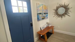 A blue door with a window, a wooden bench with a sign, a painting, and a mirror on the wall.