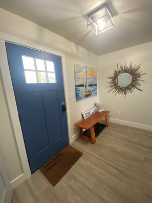 A blue door with a window, a wooden bench with a sign, a painting, and a mirror on the wall. - Stunning 4 Season New Beach House - Big Traverse Bay on Lake Superior!  (Lake Linden)