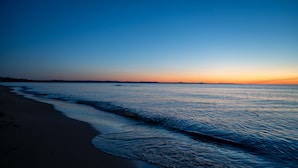 A beach with a calm sea and a clear sky during sunset.