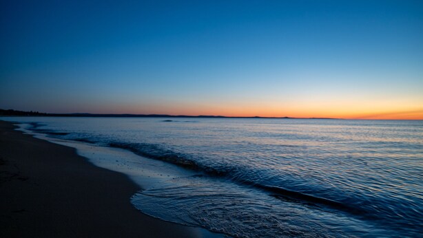 A beach with a calm sea and a clear sky during sunset.