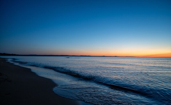 A beach with a calm sea and a clear sky during sunset. - Stunning 4 Season New Beach House - Big Traverse Bay on Lake Superior!  (Lake Linden)