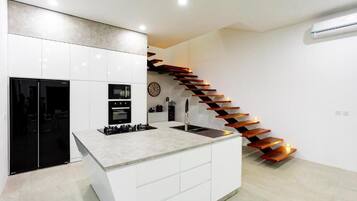 A modern kitchen with white cabinetry, a central island, a black refrigerator, and a unique wooden staircase.
