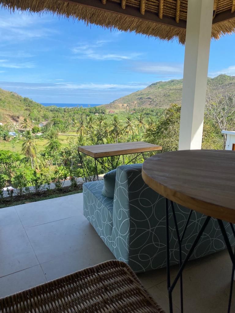 A terrace with a view of a coastal landscape, including hills and palm trees.