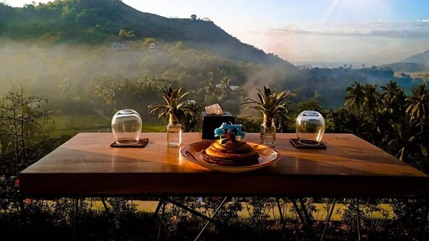 Una mesa con pastel y vasos, con vistas a un paisaje montañoso y una vista del sol.