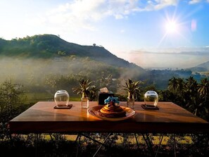 A table with a cake and glasses, overlooking a mountainous landscape with a view of the sun. - LOMBOK KHOPHILAU VILLAS (Kuta)