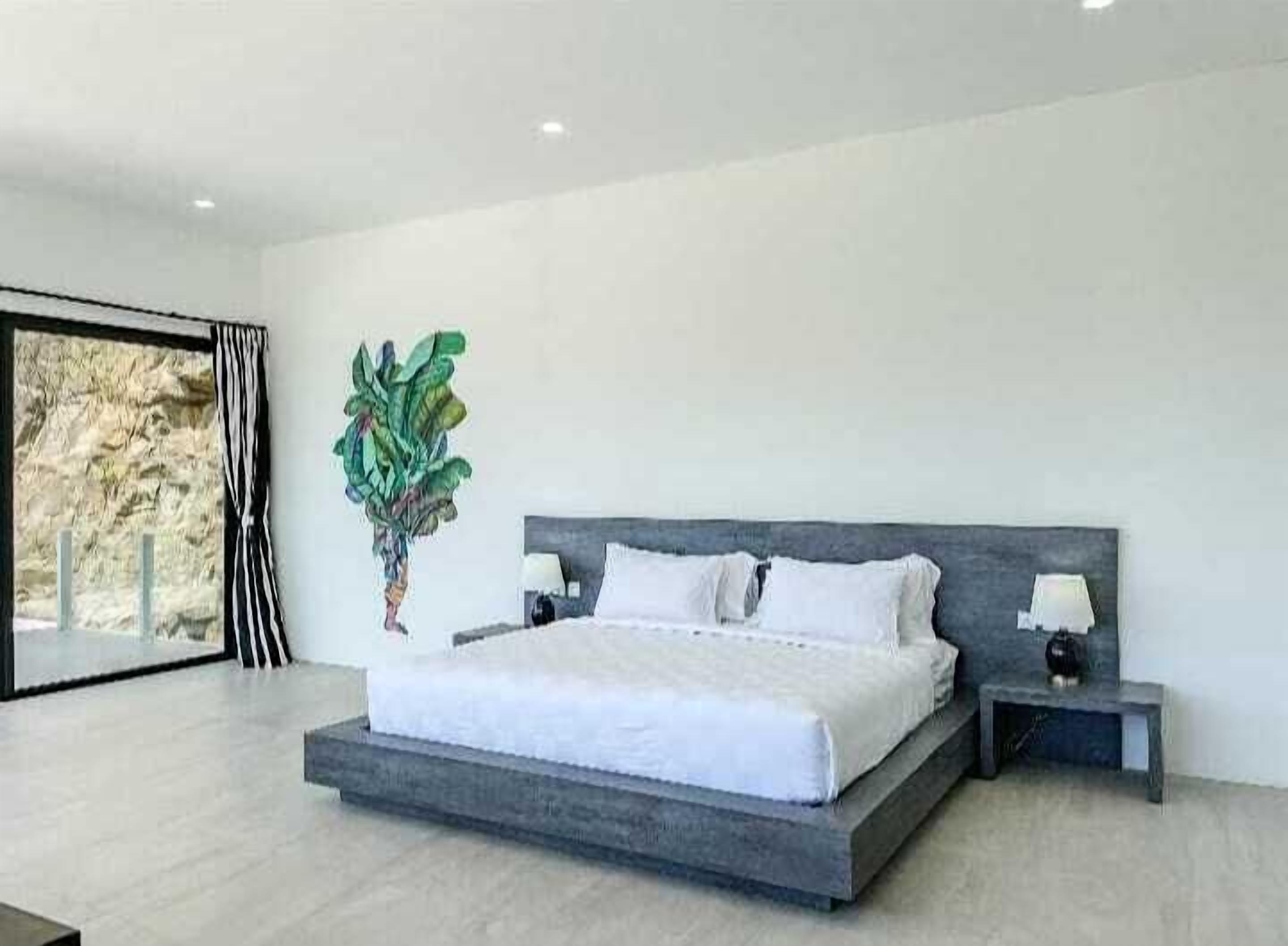 Quarto moderno com uma cama grande, mesas de cabeceira e um vaso com planta.