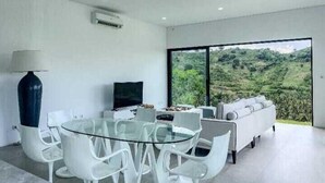 Una sala de estar moderna con una mesa de vidrio, sillas blancas, un sofá y un televisor.