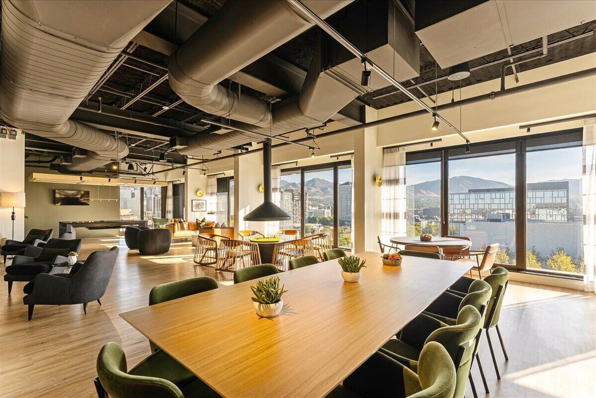 A spacious office with a large wooden table, green chairs, and potted plants.