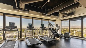 Ein Fitnessstudio mit Laufbändern, Crosstrainern und einem Ergometer, große Fenster mit Blick auf die Stadt.