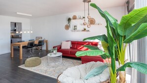 A modern living room with a red sofa, a dining area with a wooden table, and a large green plant. - Como siempre by Interhome (Vinarós)
