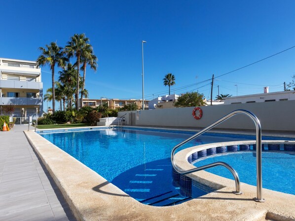 A swimming pool with a lifebuoy, palm trees, and a clear blue sky.