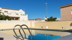 Ein Swimmingpool mit Metallgeländern, umgeben von einer beigen Mauer und einem Gebäude mit rotem Dach im Hintergrund.