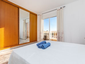 A hotel room with a large bed, a wooden wardrobe, and a sliding glass door leading to a balcony with a view of buildings.