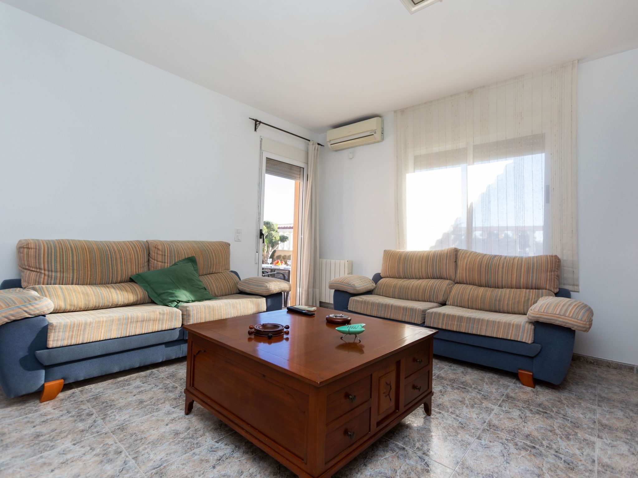 A living room with two striped sofas, a wooden coffee table, and a view through a door.