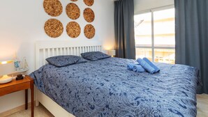 Une chambre à coucher avec un grand lit, une tête de lit blanche et un mur décoré d’œuvres d’art tissées de forme circulaire.