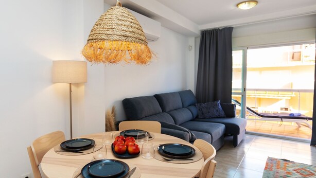 Un espace repas comprenant une table ronde en bois, des chaises et un luminaire suspendu en fibres tressées.