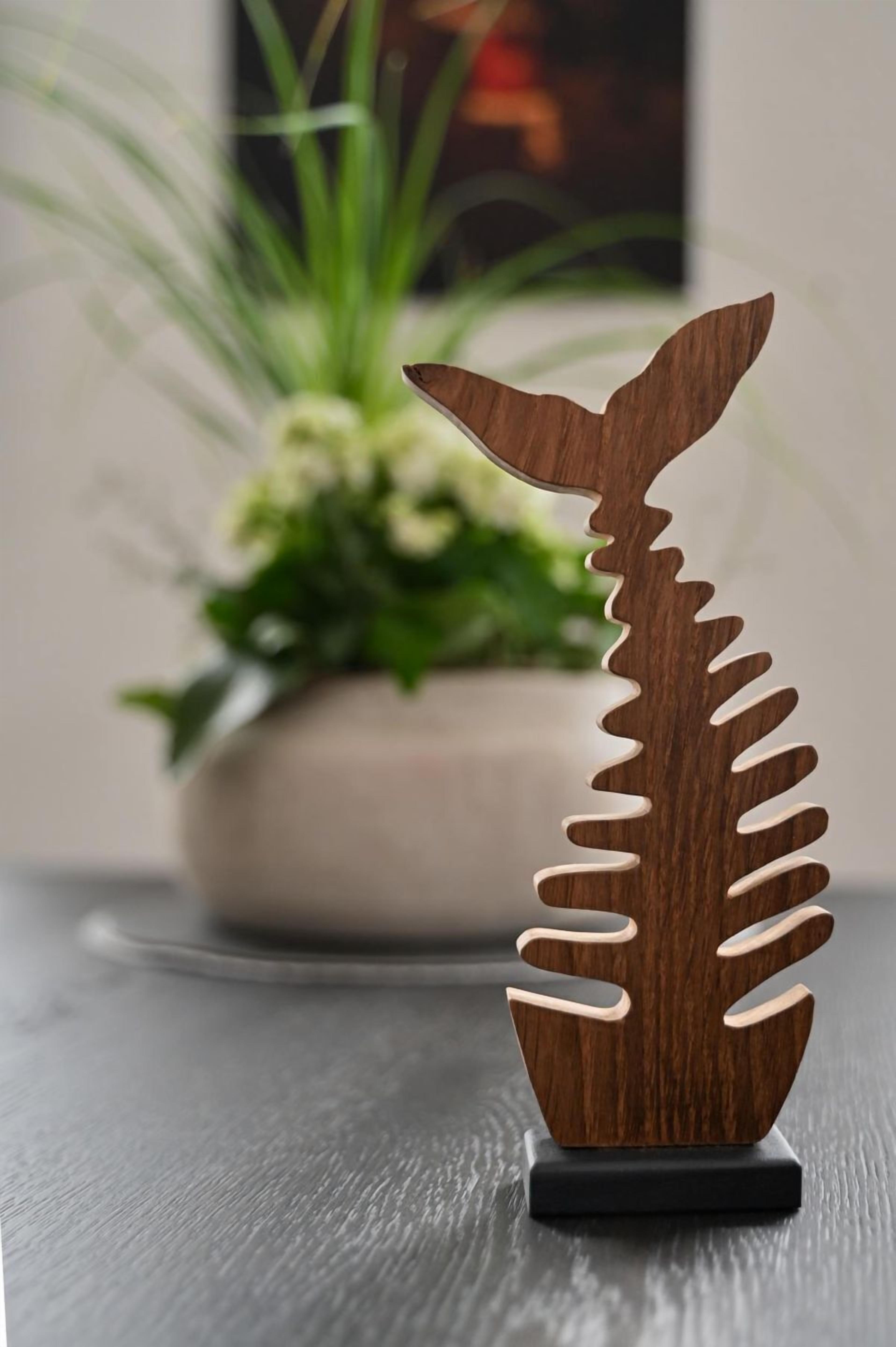 Une sculpture en bois en forme de baleine, posée sur un socle noir.