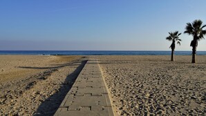 A beach with a paved walkway leading to the sea, palm trees, and clear skies. - Nova Torredembarra by Interhome (Torredembarra)