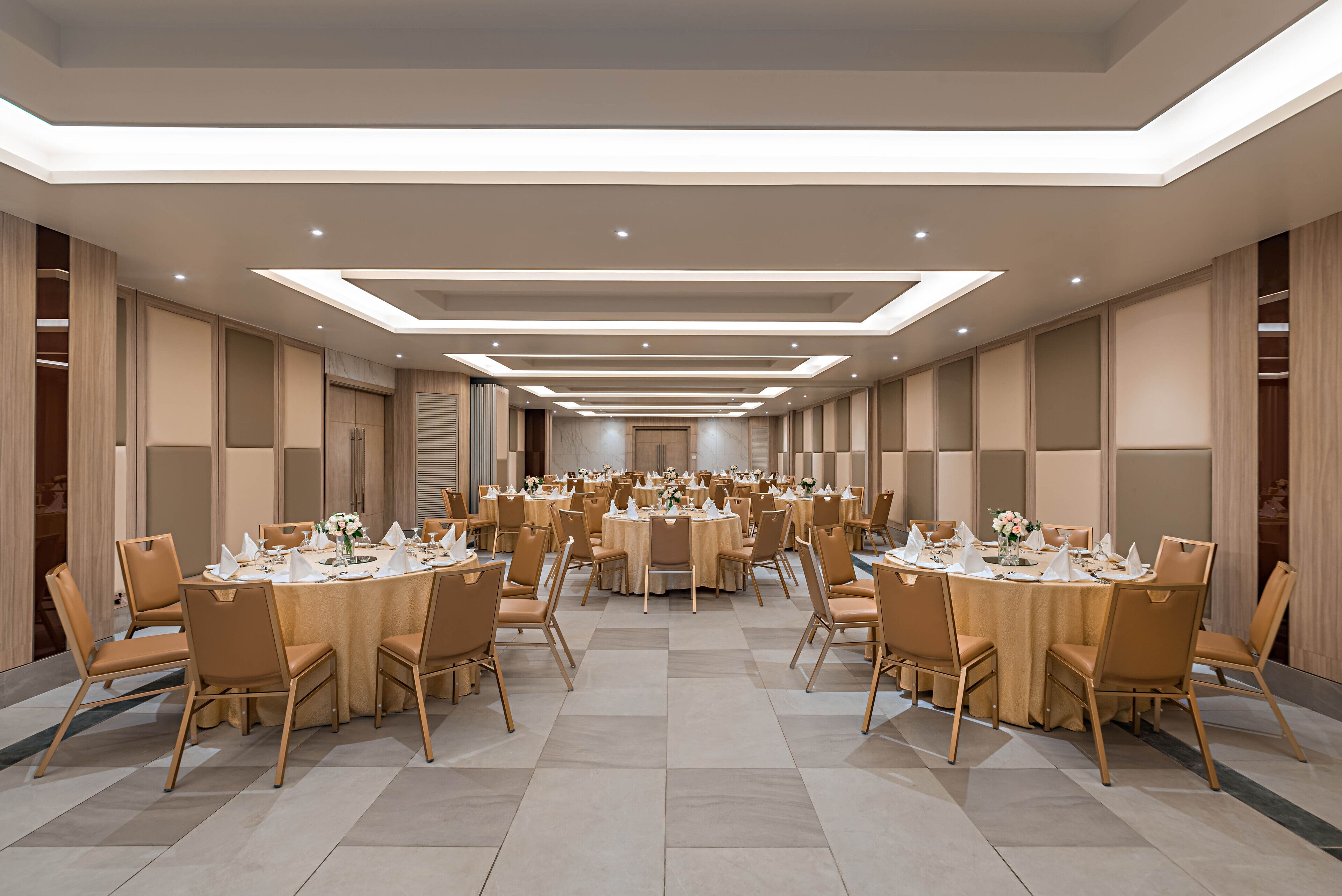 Un amplio salón de banquetes con varias mesas redondas y sillas, iluminación empotrada y un diseño de techo moderno.
