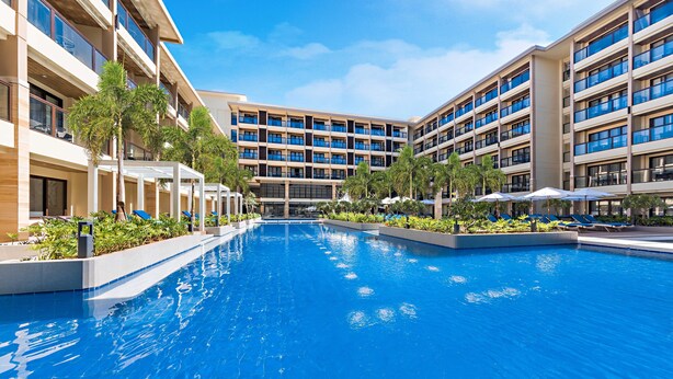Un hotel moderno con una piscina central rodeada de zonas de descanso y vegetación.