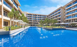 Un hotel moderno con una piscina central rodeada de zonas de descanso y vegetación.