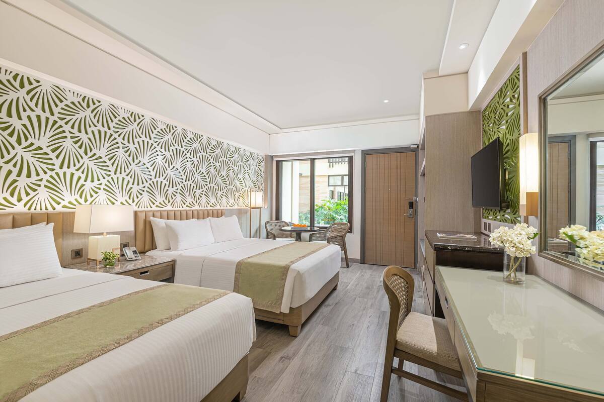 Habitación de hotel con dos camas, un escritorio, una silla, un televisor y una ventana con vistas a zonas verdes.