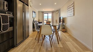 A modern kitchen with a built-in oven and refrigerator, a dining area with a glass table and chairs, and a view through a window to the outside. - ✨Gazeley Gem | Your Hamilton Hideaway Relax, Explore, Indulge (Hamilton)