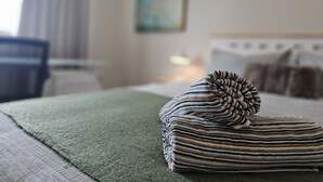 A neatly made bed with striped bedding and a green throw blanket on a textured surface. - ✨Gazeley Gem | Your Hamilton Hideaway Relax, Explore, Indulge (Hamilton)