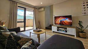A living room with a sofa, a coffee table, a TV on a stand, and a sliding glass door leading to a balcony. - ✨Gazeley Gem | Your Hamilton Hideaway Relax, Explore, Indulge (Hamilton)
