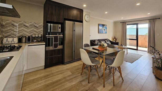 A modern kitchen with a built-in oven, microwave, and refrigerator. There is a dining area with a table and chairs, and a sofa in the living room. - ✨Gazeley Gem | Your Hamilton Hideaway Relax, Explore, Indulge (Hamilton)