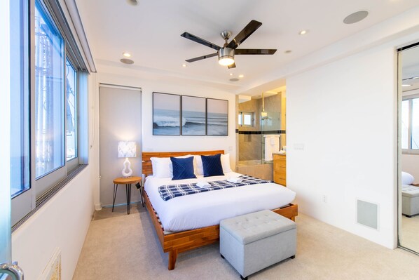 Une chambre avec un grand lit, un ventilateur de plafond et une vue sur l’océan par la fenêtre.