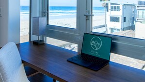 Ein Zimmer mit großem Fenster mit Blick auf einen Strand, ein Laptop auf einem Schreibtisch und ein Sessel.