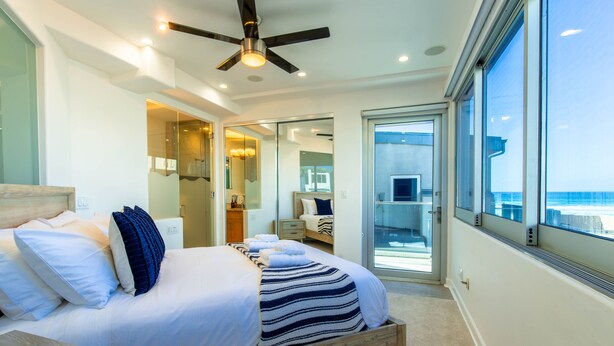 Ein modernes Schlafzimmer mit einem großen Bett, einem Deckenventilator und Meerblick durch bodengroße Fenster.