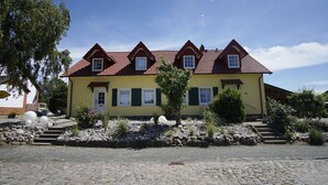 Ein gelbes Gebäude mit rotem Ziegeldach, zahlreichen Fenstern und einem Steinweg, der zum Eingang führt.