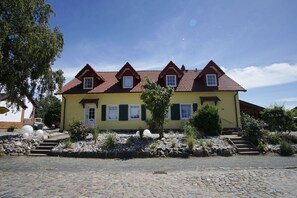 Ein gelbes Gebäude mit rotem Ziegeldach, zahlreichen Fenstern und einem Steinweg, der zum Eingang führt.