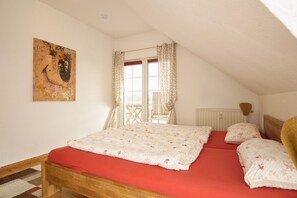 A bedroom with a wooden bed, red bedding, a window with patterned curtains, and a painting on the wall. - Viel Natur und Idyllische Umgebung - Ferienhaus Honigtopf Fewo Bernstein - Ferienhaus Honigtopf (Sagard)