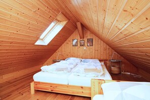 A cozy attic bedroom with a wooden sloped ceiling, a bed with white linens, a skylight, and a small shelf with a basket.