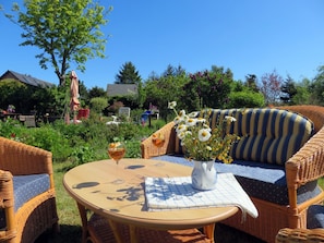 A wicker outdoor seating area with a round table, a vase with flowers, and a glass of drink. - Viel Natur und Idyllische Umgebung - Ferienhaus Honigtopf Häuschen Kormorannnest - Ferienhaus (Sagard)