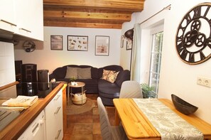 A compact living space with a kitchenette, a sofa, a dining table, and a large wall clock.