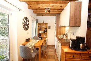 Una cocina compacta con armarios de madera, una mesa de comedor con sillas y una cafetera.