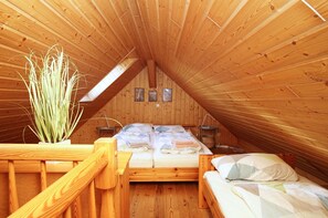Een knus slaapkamer op zolder, met houten wanden, een schuine plafond en een bed met veel kussens.