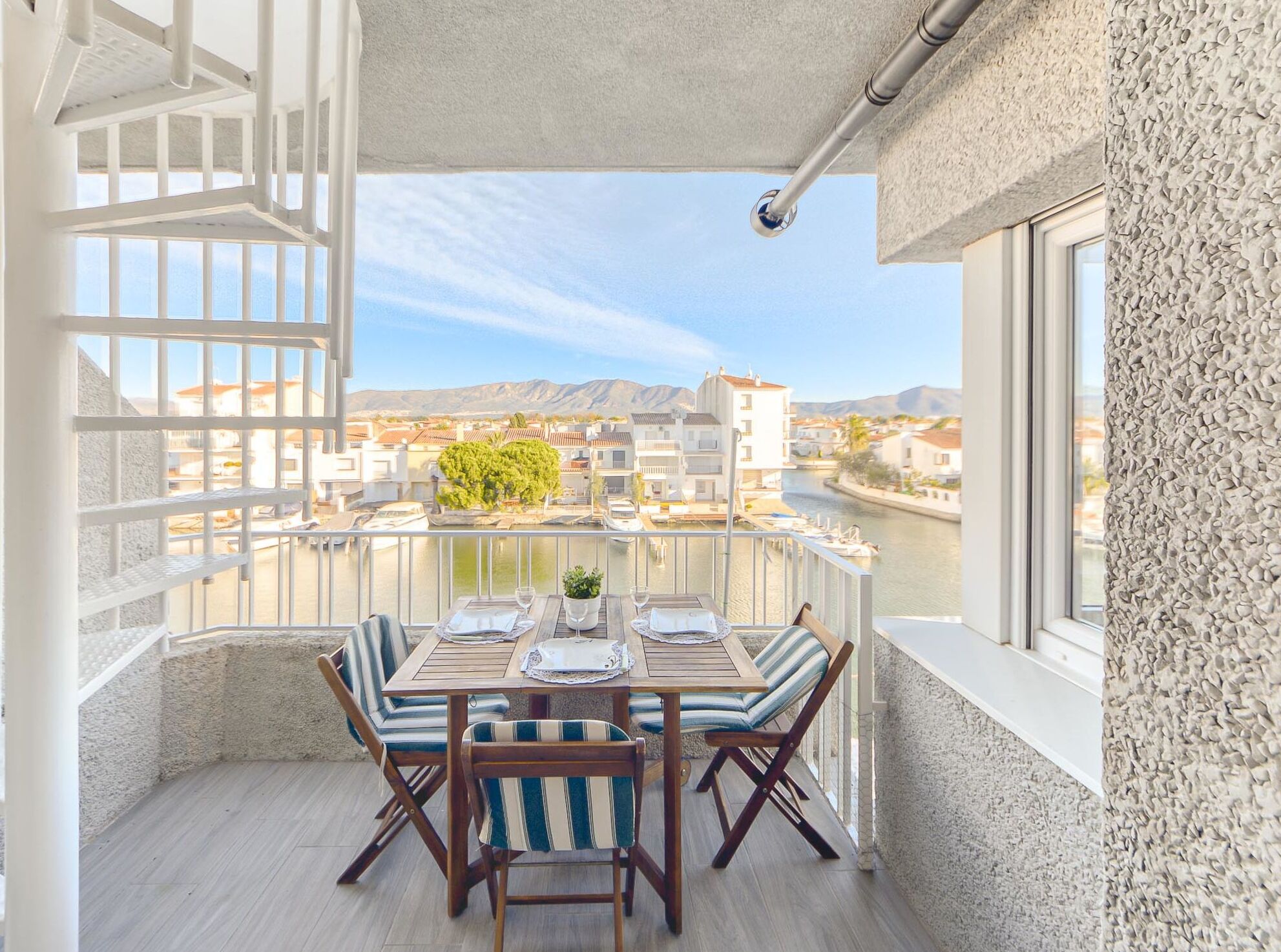 A balcony with a table set for two, overlooking a river and buildings.