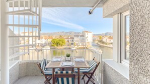 A balcony with a table set for two, overlooking a river and buildings. - Onada I by Interhome (Empuriabrava)
